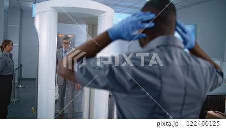 Mature Businessman Passes Through Metal Detector Scanner. Security Officer Inspects Passenger Mature Businessman Passes Through Metal Detector Scanner. Security Officer Inspects Passenger 122460125