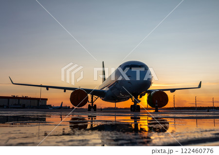Modern passenger plane on the airport against the backdrop of a scenic sunrise with reflection in a puddle Modern passenger plane on the airport against the backdrop of a scenic sunrise with reflection in a puddle 122460776