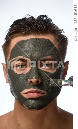 Man with smooth skin looking directly forward, and hand wearing black glove holding brush, mask covering most of face against white studio background. 122461618