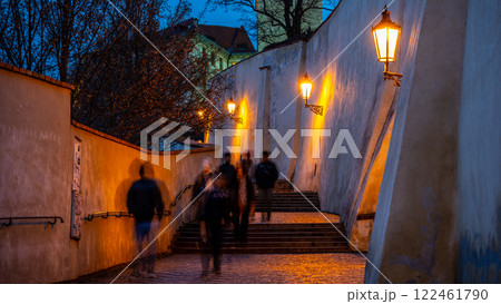 Visitors walk down a beautifully lit staircase at Prague Castle during dusk. The old stone steps are lined with warm lamps, creating a magical atmosphere in the historic setting. Visitors walk down a beautifully lit staircase at Prague Castle during dusk. The old stone steps are lined with warm lamps, creating a magical atmosphere in the historic setting. 122461790