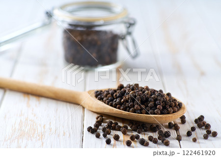 black pepper seeds in a wooden scoop and in glass storage jar on a white wooden table, selective focus. 122461920