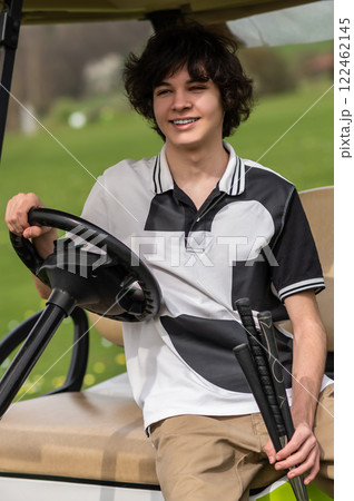 Handsome young golfer riding a gold cart and looking contented Handsome young golfer riding a gold cart and looking contented 122462145