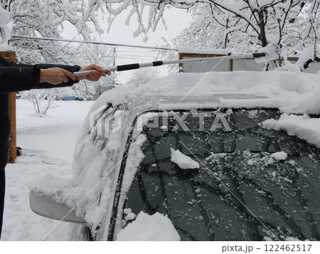 hands with an extended scraper scraping fresh snow from the roof of a silver car against the background of snowy trees, clearing snow-covered personal transport by a driver using a device hands with an extended scraper scraping fresh snow from the roof of a silver car against the background of snowy trees, clearing snow-covered personal transport by a driver using a device 122462517