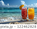 two different cocktails stand in the sand on the edge of the water on a perfect beach in the sand against the backdrop of the blue ocean. 122462828
