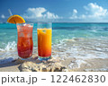 two different cocktails stand in the sand on the edge of the water on a perfect beach in the sand against the backdrop of the blue ocean. 122462830