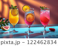 Still life of three bright yellow and red drinks in different glasses against the backdrop of a blue pool and golden sand in a neon style. 122462834