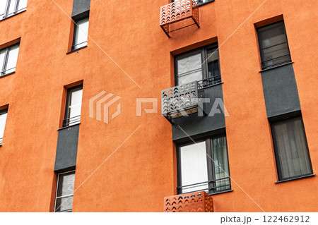 Contemporary apartment building with orange facades with dark-framed windows and decorative metal grille for air conditioner Contemporary apartment building with orange facades with dark-framed windows and decorative metal grille for air conditioner 122462912