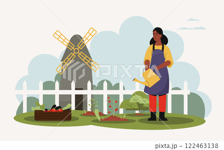 Young woman farmer wearing apron and watering plants in her vegetable garden with tomatoes, lettuce and eggplants growing near a wooden crate and a windmill in background Young woman farmer wearing apron and watering plants in her vegetable garden with tomatoes, lettuce and eggplants growing near a wooden crate and a windmill in background 122463138