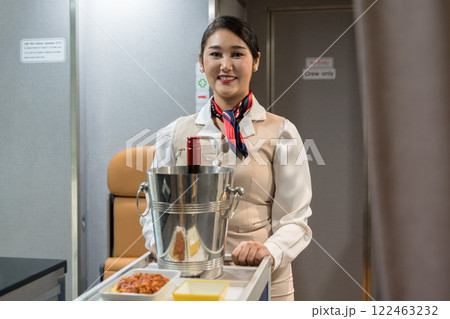 Smiling Asian flight attendant holding food and beverage cart in aircraft cabin for serving passengers Smiling Asian flight attendant holding food and beverage cart in aircraft cabin for serving passengers 122463232