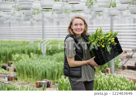 Young woman standing in greenhouse with box with tulips. Concept work in the greenhouse 122463646