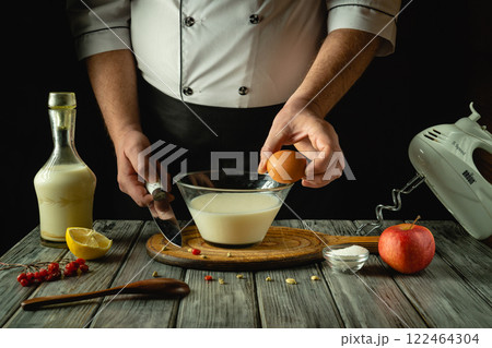 Hands skillfully prepare a mixture in a glass bowl, combining egg, milk, and lemon. Fresh apples and a wooden board enhance the inviting atmosphere of this culinary creation 122464304
