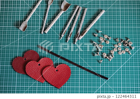 Tanners green cutting mat with work tools and red leathers hearts, close-up, selective focus. 122464311