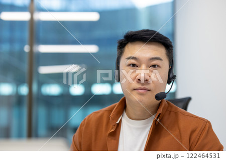 Asian man businessman with headset in office focused on digital communication. Shows modern work environment, casual attire, professional engagement. Represents tech-savvy business practices. Asian man businessman with headset in office focused on digital communication. Shows modern work environment, casual attire, professional engagement. Represents tech-savvy business practices. 122464531