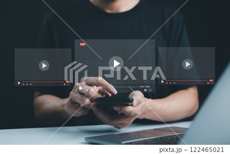Live streaming and video content creation concept. A man uses a smartphone device with transparent video player interfaces, symbolizing live streaming, digital media, and video content creation. Live streaming and video content creation concept. A man uses a smartphone device with transparent video player interfaces, symbolizing live streaming, digital media, and video content creation. 122465021