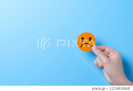 Sad Face Emoji Representing Negative Emotion. A hand holding sad face emoji, symbolizing negative emotions, dissatisfaction, and an unhappy customer experience. emotional or feedback related concepts. 122465068