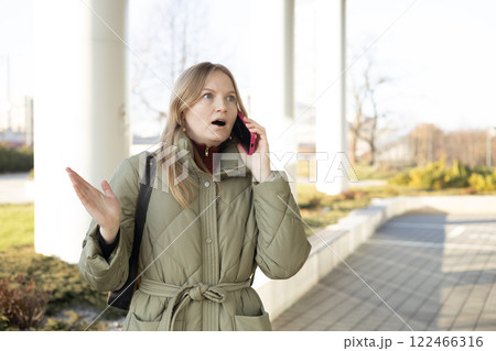 Portrait of beautiful shocked young woman talking on the mobile as she getting terrible news on the city street 122466316