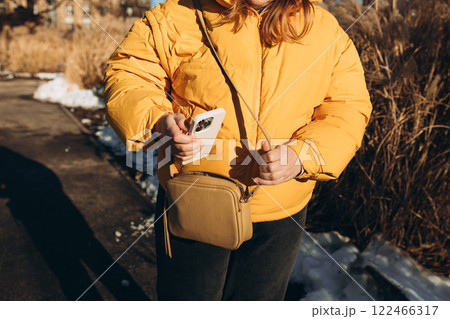 Closeup of woman's hands taking out smartphone from purse outdoors. Young stylish woman taking cellphone out of handbag. Crop anonymous female putting modern cellphone into fashionable handbag 122466317