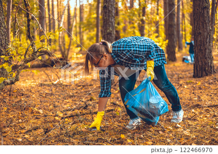 A woman volunteer collects plastic waste in the forest. A woman saves nature from being polluted by garbage. Environmental problems, plastic waste, environmental pollution. 122466970