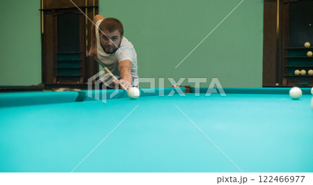 Cute man aiming a cue at a billiard ball. In the evening, a man relaxes and relaxes while playing billiards. A man hits the ball with a cue, aiming for a pocket on a billiard table. Cute man aiming a cue at a billiard ball. In the evening, a man relaxes and relaxes while playing billiards. A man hits the ball with a cue, aiming for a pocket on a billiard table. 122466977