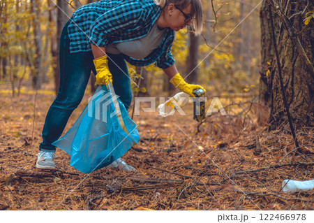 A woman fights to save the forest from garbage. A woman with a garbage bag in her hands collects plastic waste in the forest. Ecology, saving nature from plastic waste. A woman fights to save the forest from garbage. A woman with a garbage bag in her hands collects plastic waste in the forest. Ecology, saving nature from plastic waste. 122466978