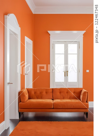 A living room sofa is positioned against an orange wall, with a white classic door in background 122467348