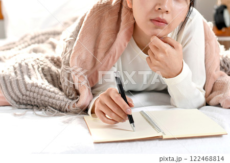 ベッドの上でメモを書き考える若い女性 122468814