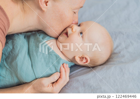 A mother gently wraps her baby in a soft muslin swaddle, providing warmth and comfort. A tender moment of care and love between mother and child. Motherhood, baby care, and nurturing concept 122469446