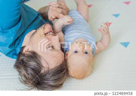 A loving father lies next to his 3-month-old baby, safely secured in a cozy infant cocoon with a special safety belt. Heartwarming family bonding moment. Parenthood, love, and baby care concept A loving father lies next to his 3-month-old baby, safely secured in a cozy infant cocoon with a special safety belt. Heartwarming family bonding moment. Parenthood, love, and baby care concept 122469458
