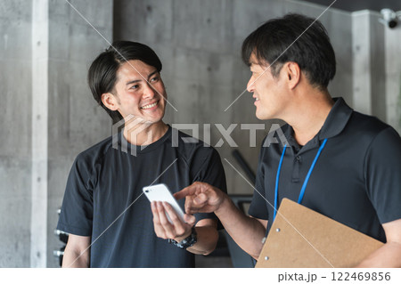 パーソナルトレーニングでカウンセリングを受ける若いアジア人男性とパーソナルトレーナーの男性 122469856