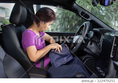 Senior asian woman sitting on drivers seat and look for a key inside handbag. 122470251
