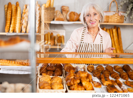 Elderly bakery saleswoman places fresh croissants on display 122471065