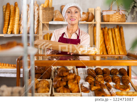 Mature woman seller took fresh loaves of white flour out of window in bakery 122471087