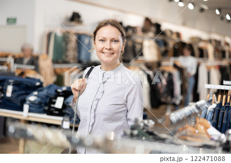 Middle-aged woman watching excitedly large stock of clothes in clothing store 122471088