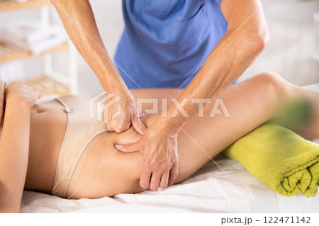 Image showcases close-up of mature female masseur hands skillfully working on things hip of woman 122471142