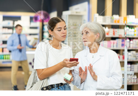 Young girl showing to old pharmacist QR-code of product on her smartphone Young girl showing to old pharmacist QR-code of product on her smartphone 122471171