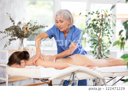 Elderly woman doing back massage to young woman 122471229