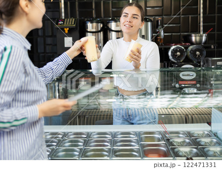 Smiling young saleswoman extending cups of bubble tea to female customer 122471331