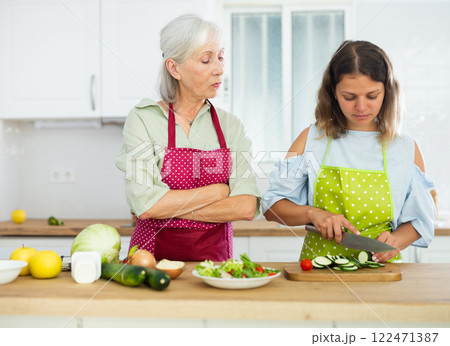 Elderly mother teaching adult daughter how to cook vegetable salad in kitchen 122471387