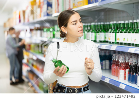 Girl customer is thinking about buying spicy and unusual Korean soy wine chum churum. 122471492