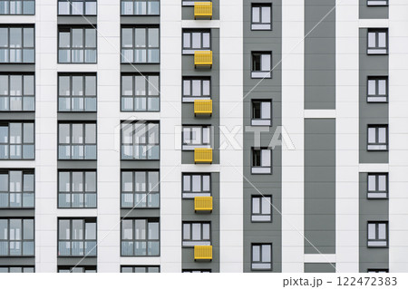 Contemporary building facade with yellow and grey accents, minimalist design, windows, and balconies, against a cloudy sky, front close view Contemporary building facade with yellow and grey accents, minimalist design, windows, and balconies, against a cloudy sky, front close view 122472383