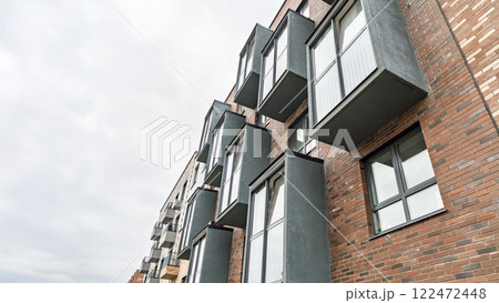 Contemporary apartment facade with multicolored brick walls, windows, and protruding grey balconies. Urban housing concept, low angle view Contemporary apartment facade with multicolored brick walls, windows, and protruding grey balconies. Urban housing concept, low angle view 122472448