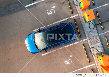 Blue electric car receives electricity at parking lot with charging station stands upper view. Modern eco-friendly auto reveals benefit of low cost fuel Blue electric car receives electricity at parking lot with charging station stands upper view. Modern eco-friendly auto reveals benefit of low cost fuel 122473243