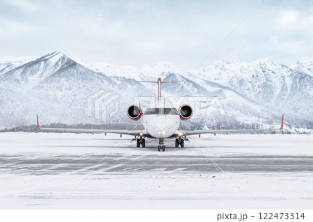 Front view of a passenger regional jet taxiing at winter airport on the background of high scenic mountains 122473314