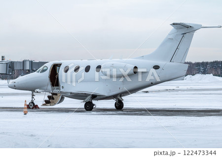 Modern white business jet with an opened gangway door at the winter airport apron 122473344