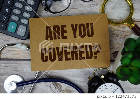 Are You Covered? text with calculator, magnifying glass and alarm clock on wooden background 122473375
