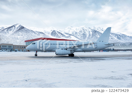White passenger plane taxiing on the airport at winter on the background of high scenic mountains White passenger plane taxiing on the airport at winter on the background of high scenic mountains 122473429