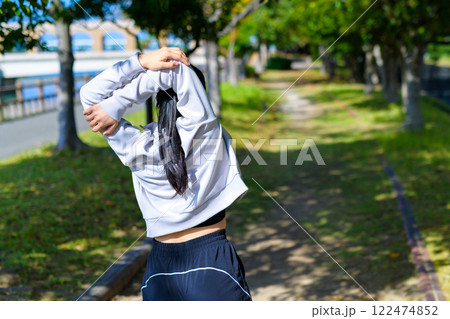 肩甲骨ストレッチ　木漏れ日の道で肩のストレッチをするかっこいい女性　ダイエット　トリミングアップ 122474852