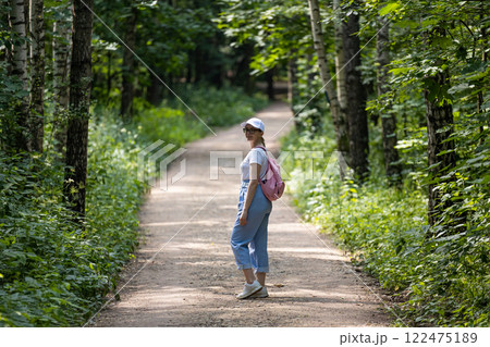 Exploring a tranquil woodland path on a sunny day with casual attire and a joyful demeanor 122475189