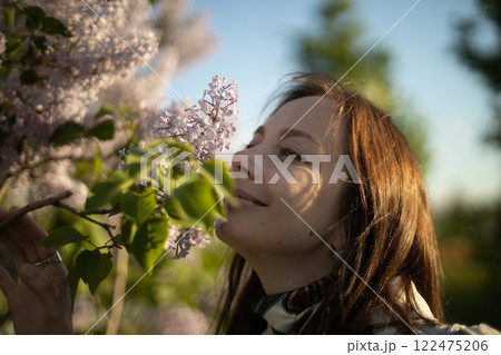 Woman enjoying the fragrance of blooming lilacs in a sunlit garden during springtime Woman enjoying the fragrance of blooming lilacs in a sunlit garden during springtime 122475206