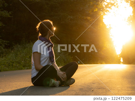 Sunset tranquility as a woman sits peacefully on a quiet road surrounded by natures glow 122475209